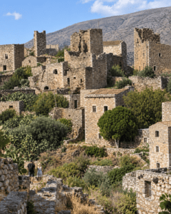 Τρία άτομα απολαμβάνουν ελαφρύ πικνίκ στην πλατεία της Αρεόπολης, με πετρόχτιστα κτίρια στο φόντο